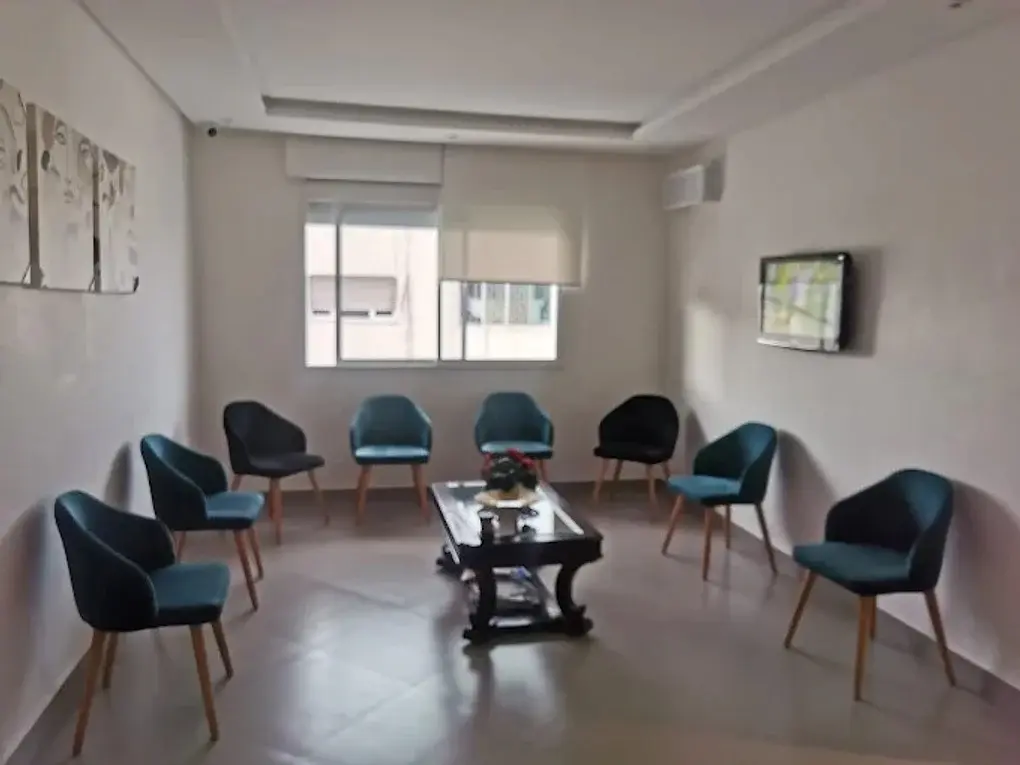 Salle d'attente du cabinet : fauteuils bleu canard autour d'une table basse, lumière naturelle