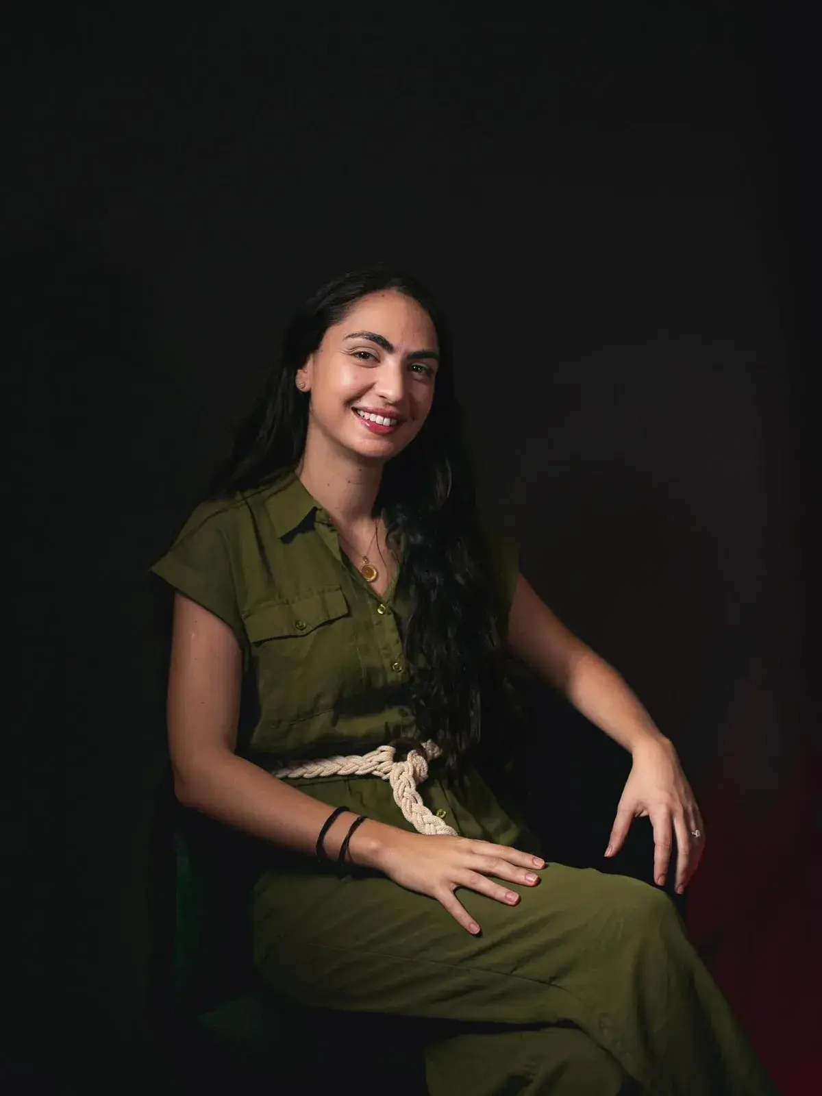 Portrait du Dr Jihane Benahmed, dermatologue à Rabat, souriante, en combinaison vert olive sur fond sombre